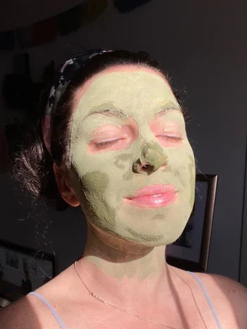A woman enjoying a relaxing self-care moment with a green matcha face mask, sunlight softly highlighting her serene expression.
