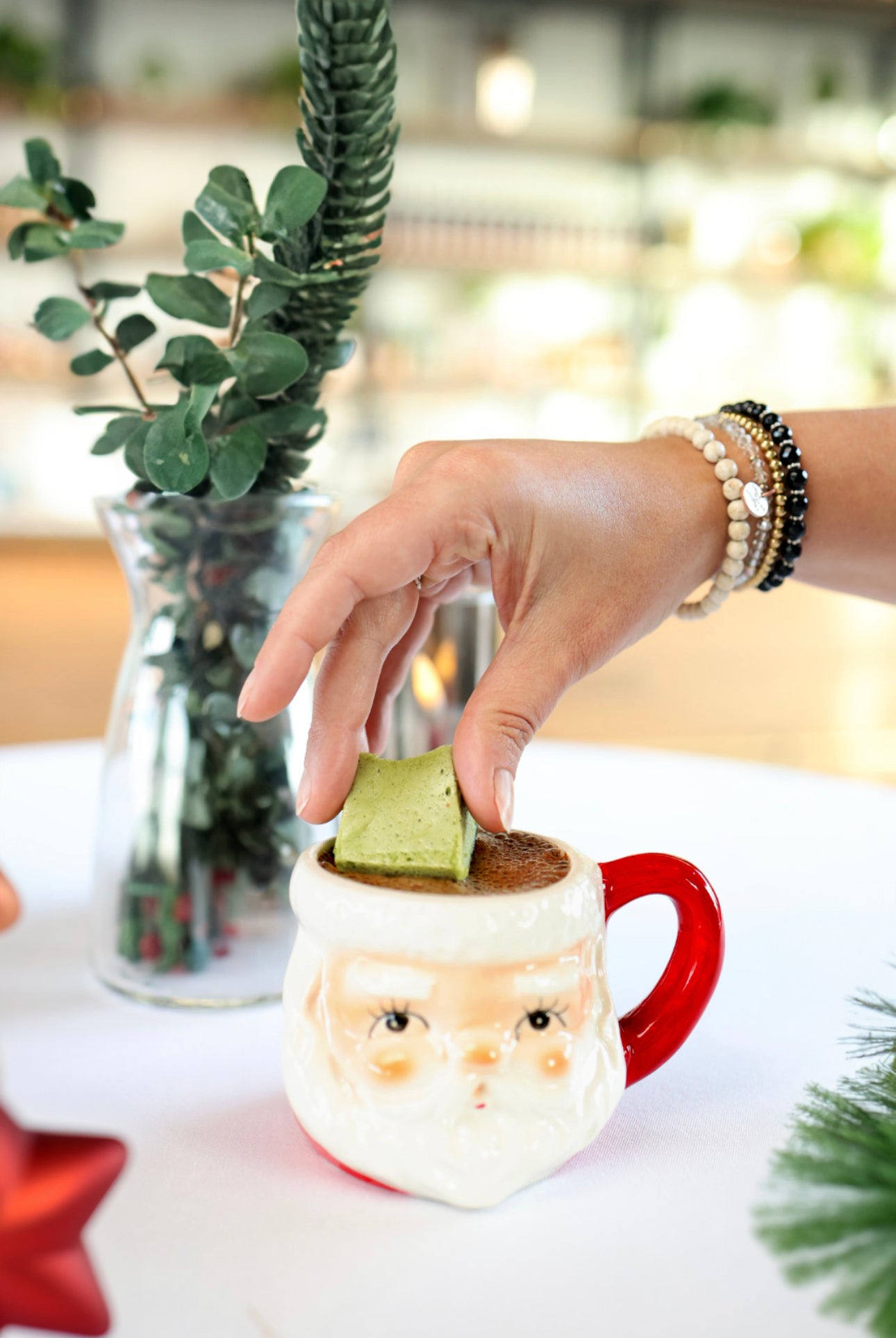 A festive Santa mug filled with rich dairy-free hot cocoa, topped with a vibrant green matcha marshmallow, surrounded by holiday greenery and cozy winter decor.