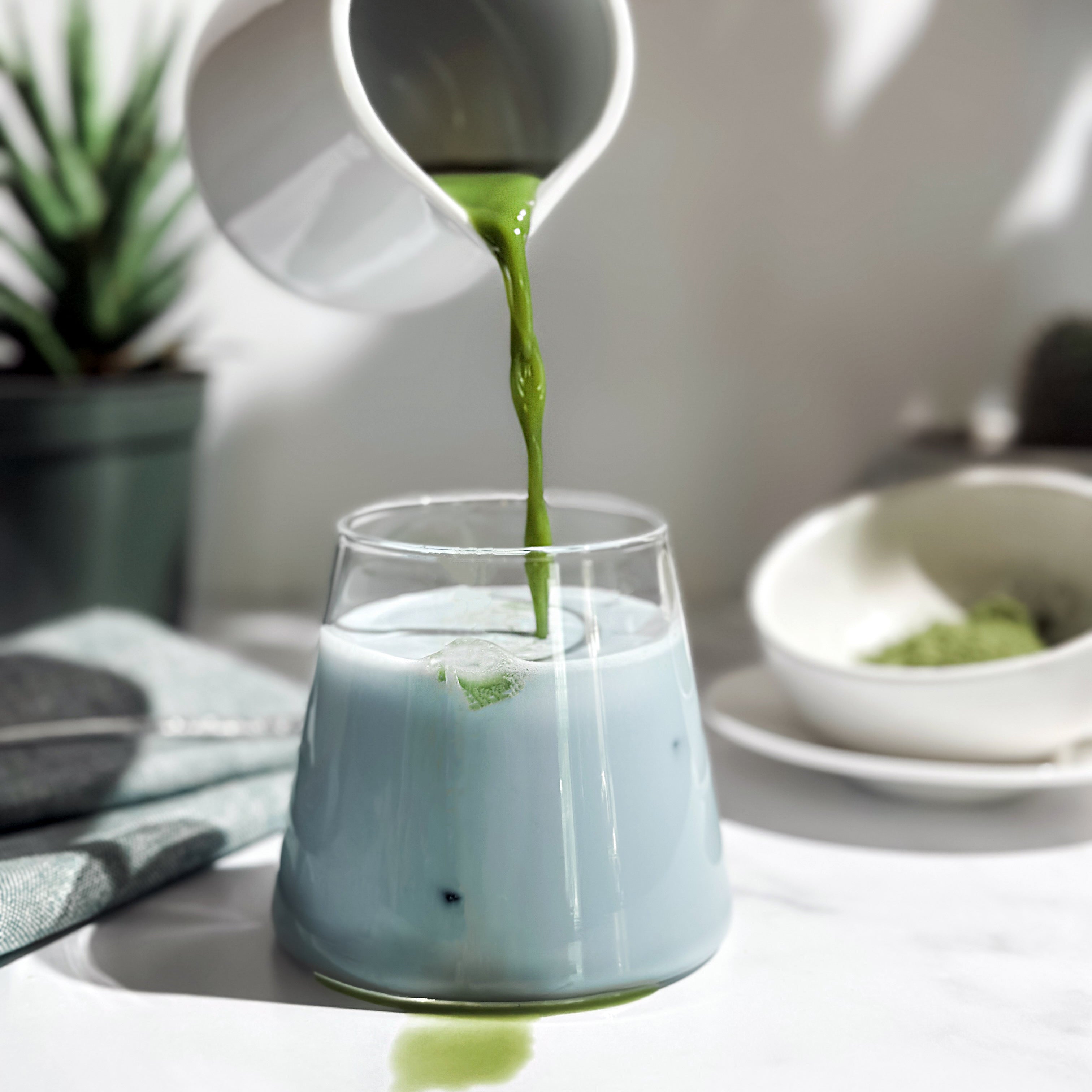 A vibrant Earth Day Matcha Latte in a glass, layered with mint tea, creamy plant-based milk, and a bright green matcha shot, surrounded by fresh greenery for a sustainable and refreshing vibe.