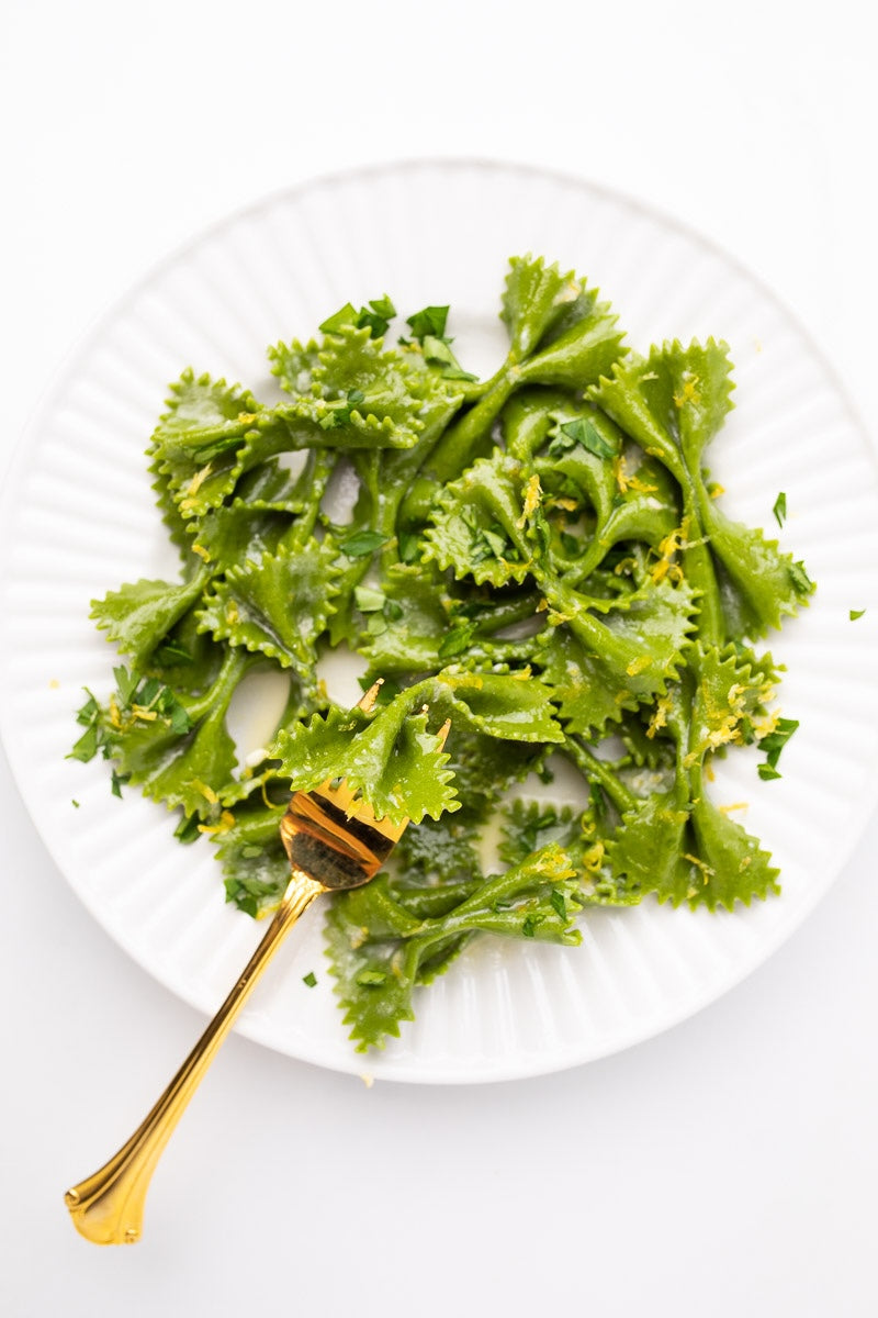 Vibrant green matcha pasta topped with zesty lemon butter sauce, garnished with parsley and grated Parmesan, elegantly plated on a white dish