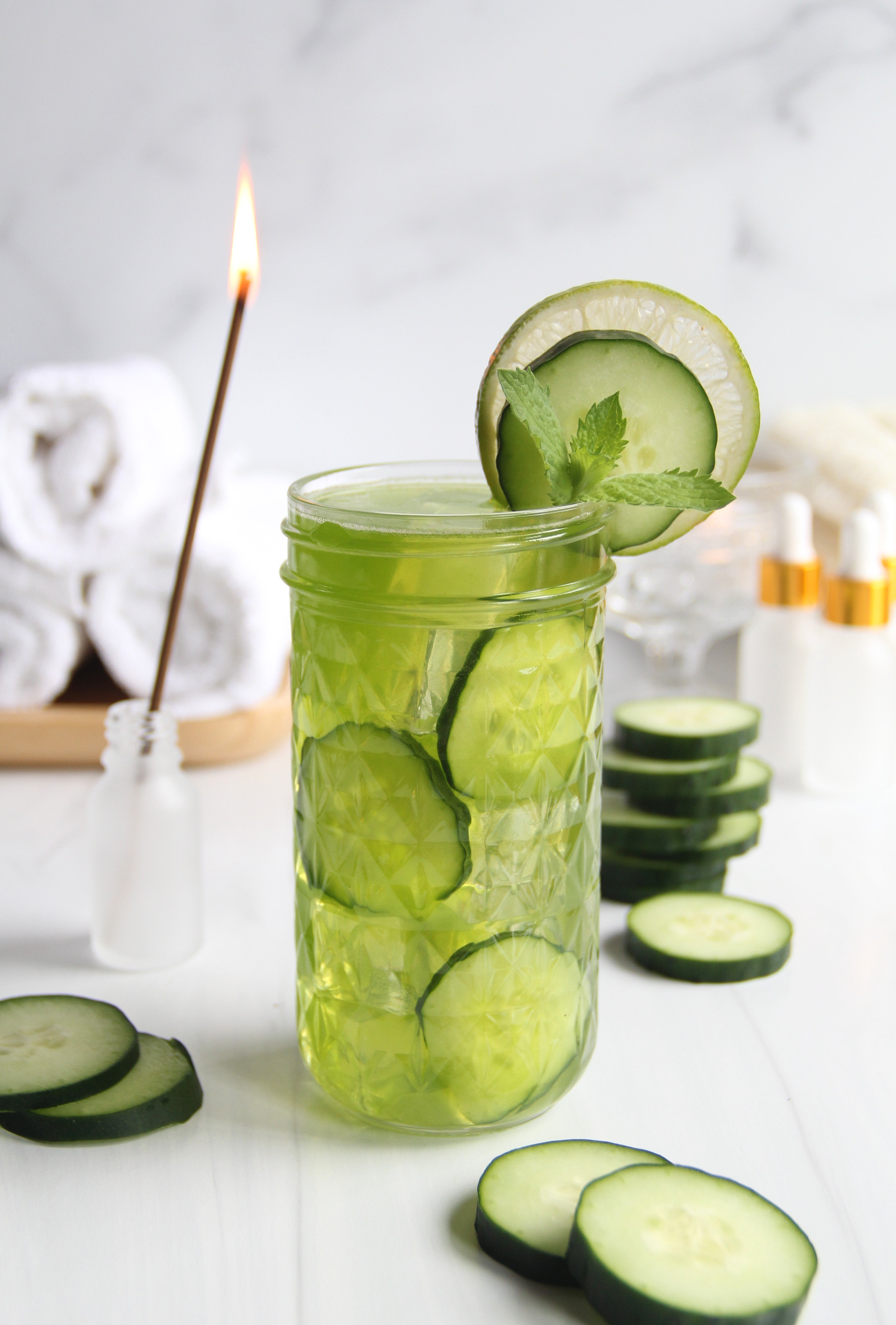 Refreshing Matcha Cucumber Lime Refresher served in a textured glass with cucumber slices, lime, and mint garnish, styled with spa-inspired elements in the background