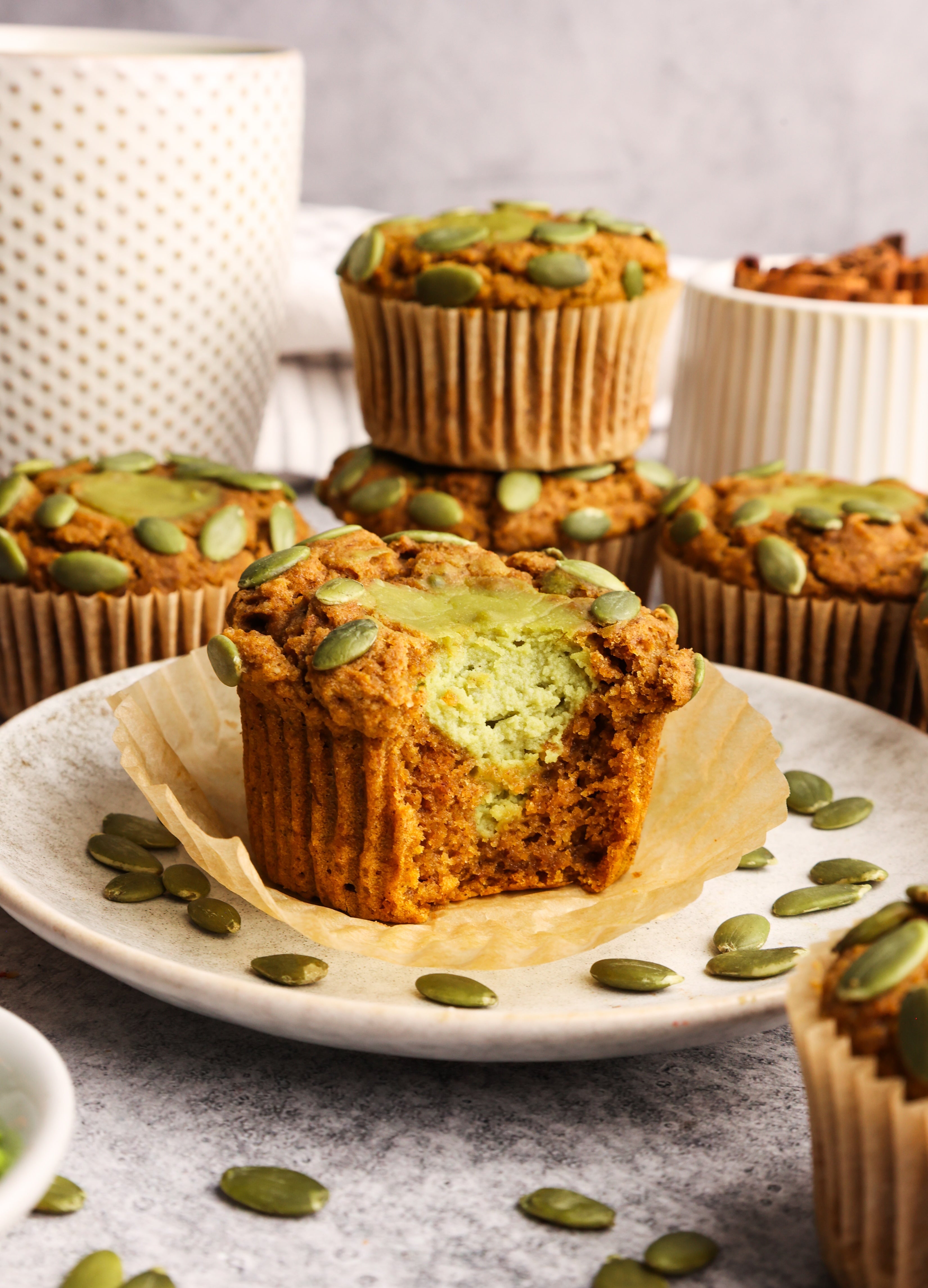 Gluten-free pumpkin muffins with matcha cream cheese filling topped with pumpkin seeds on a cooling rack