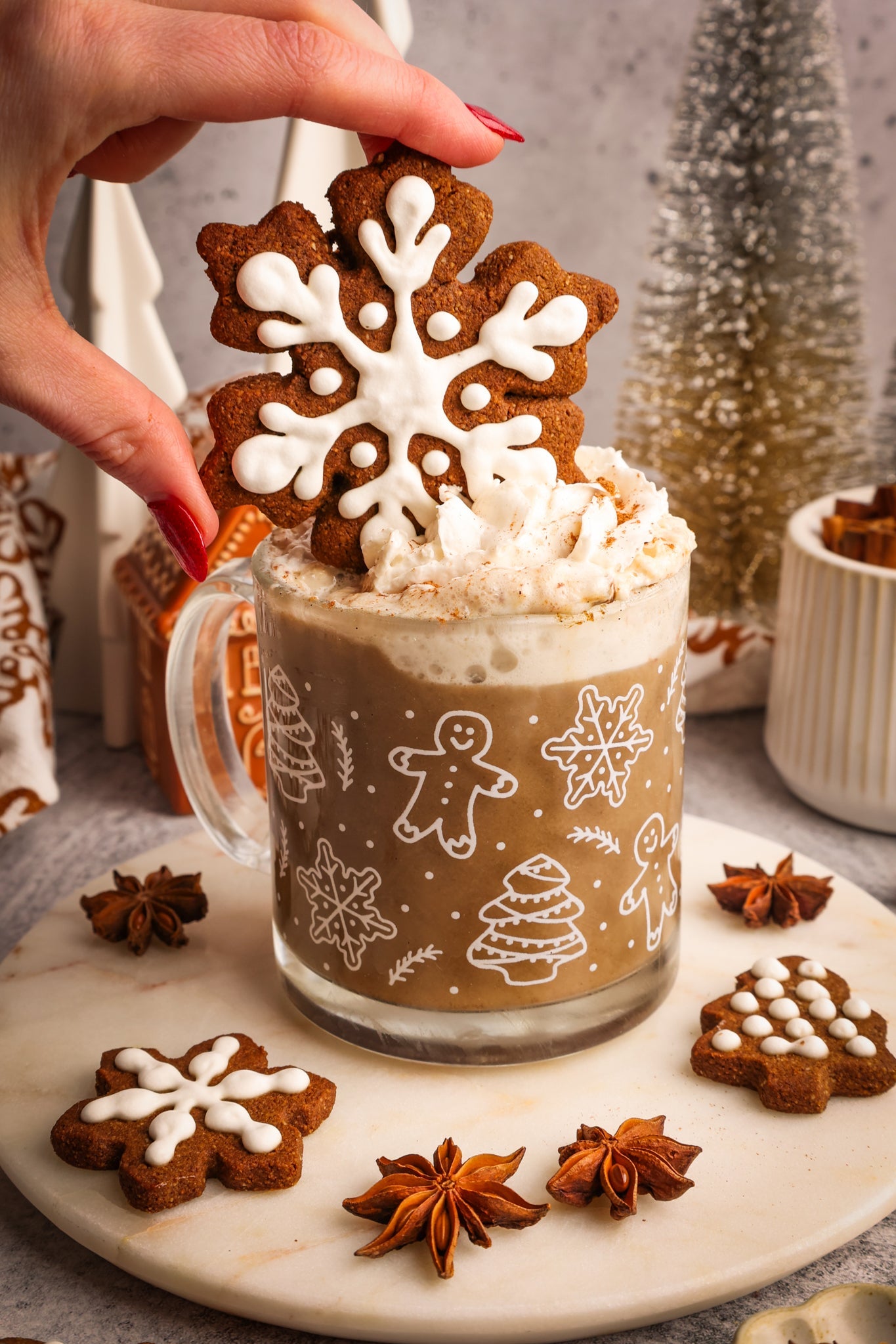 A festive gingerbread hojicha latte topped with whipped cream and a snowflake gingerbread cookie, surrounded by star anise and holiday décor.