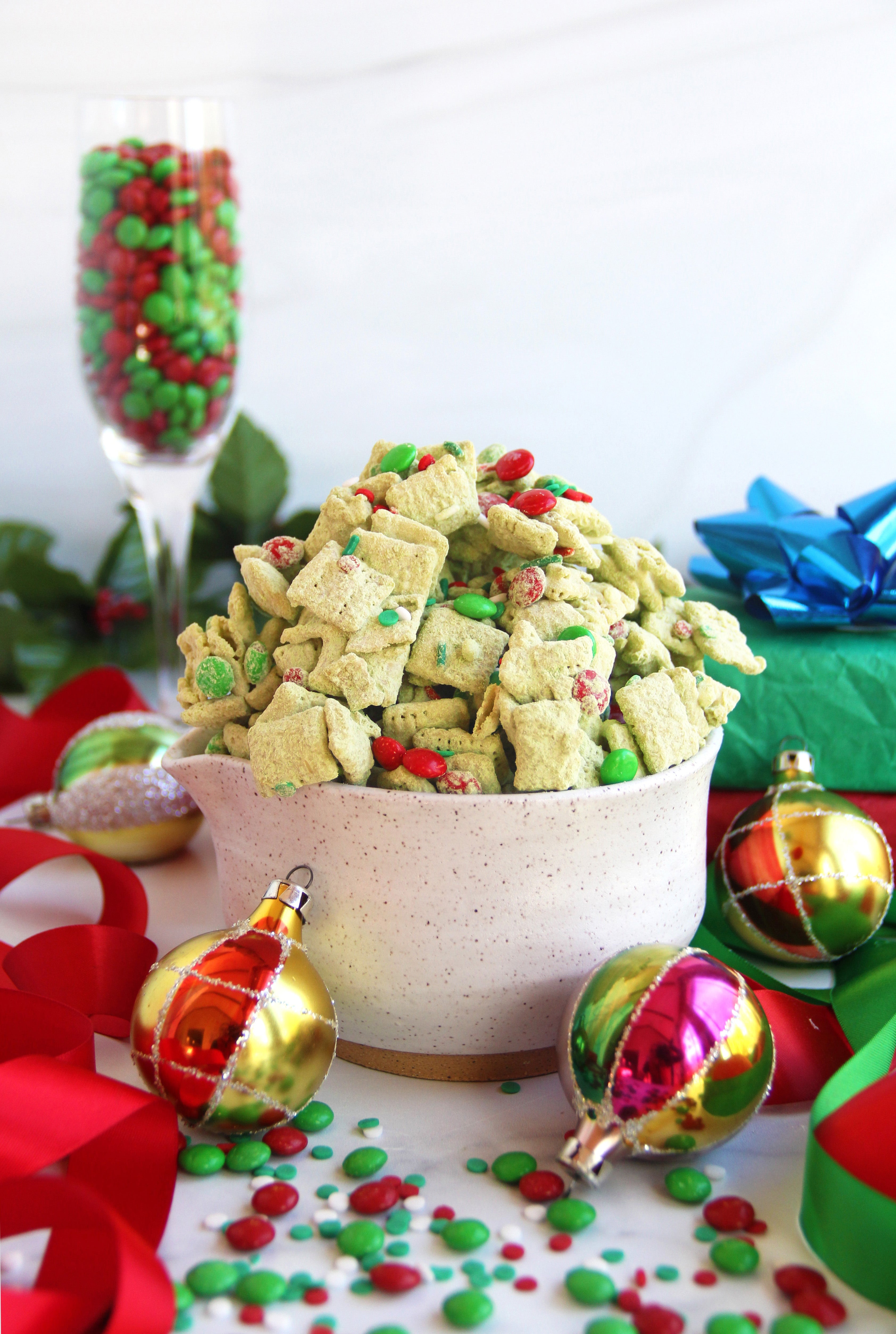 Bowl of festive green Matcha Puppy Chow surrounded by red and green Christmas candies and ornaments