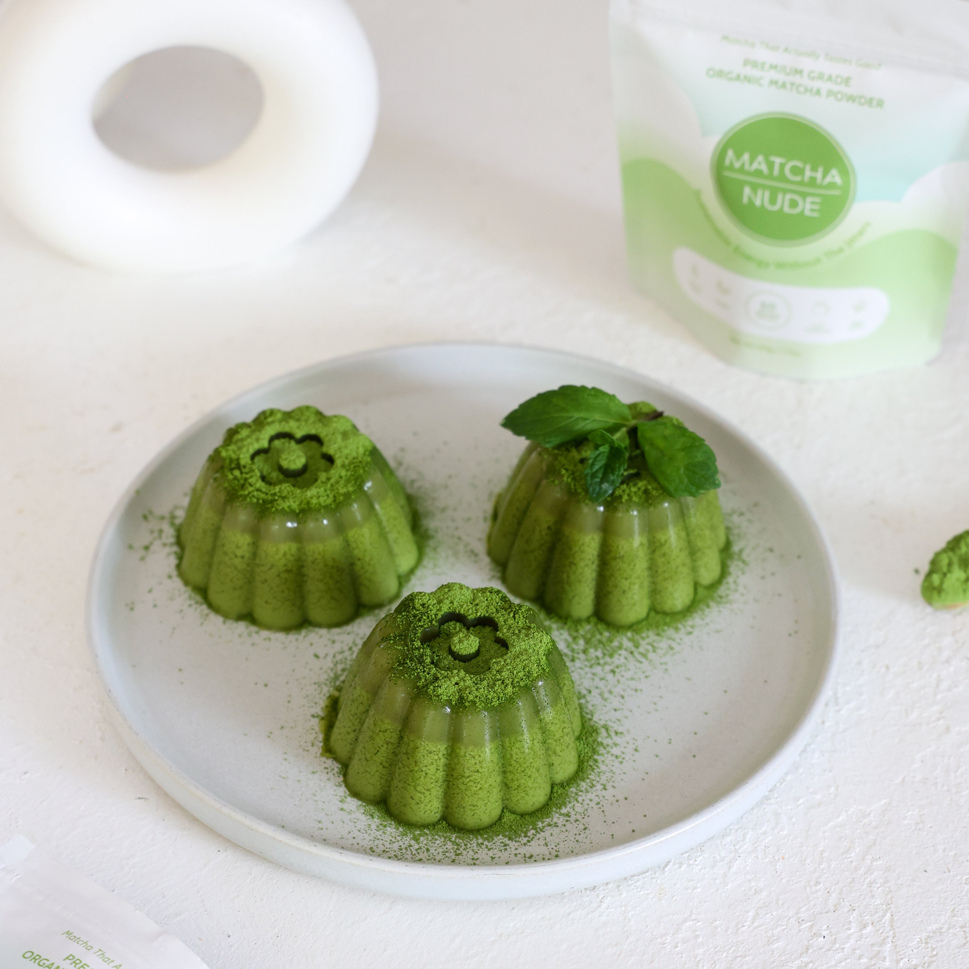 Green matcha panna cotta garnished with fresh mint on a ceramic plate.