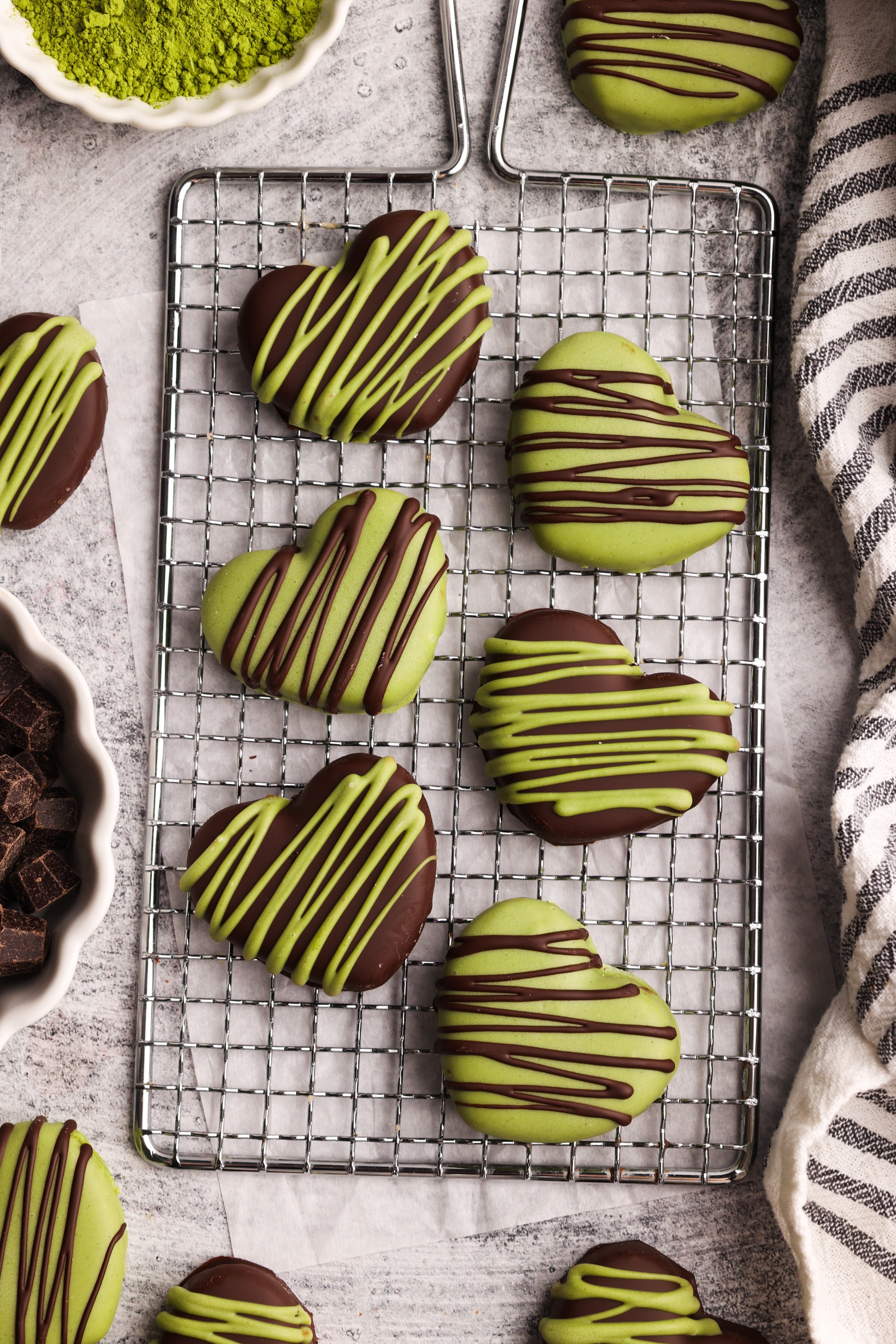 Heart-shaped no-bake matcha cashew butter cookies drizzled with dark and white chocolate on a cooling rack