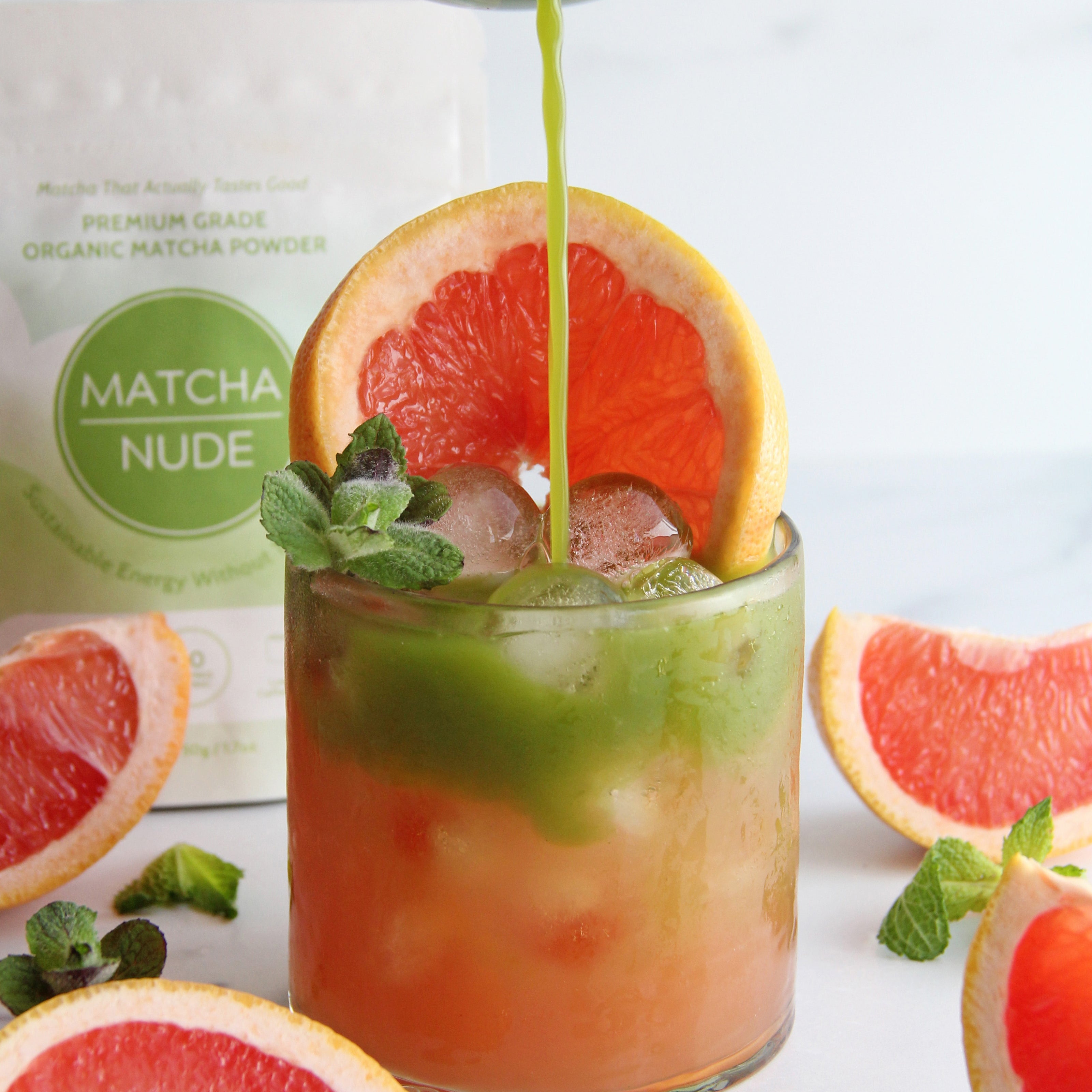 Matcha being poured over a grapefruit paloma drink with ice and mint