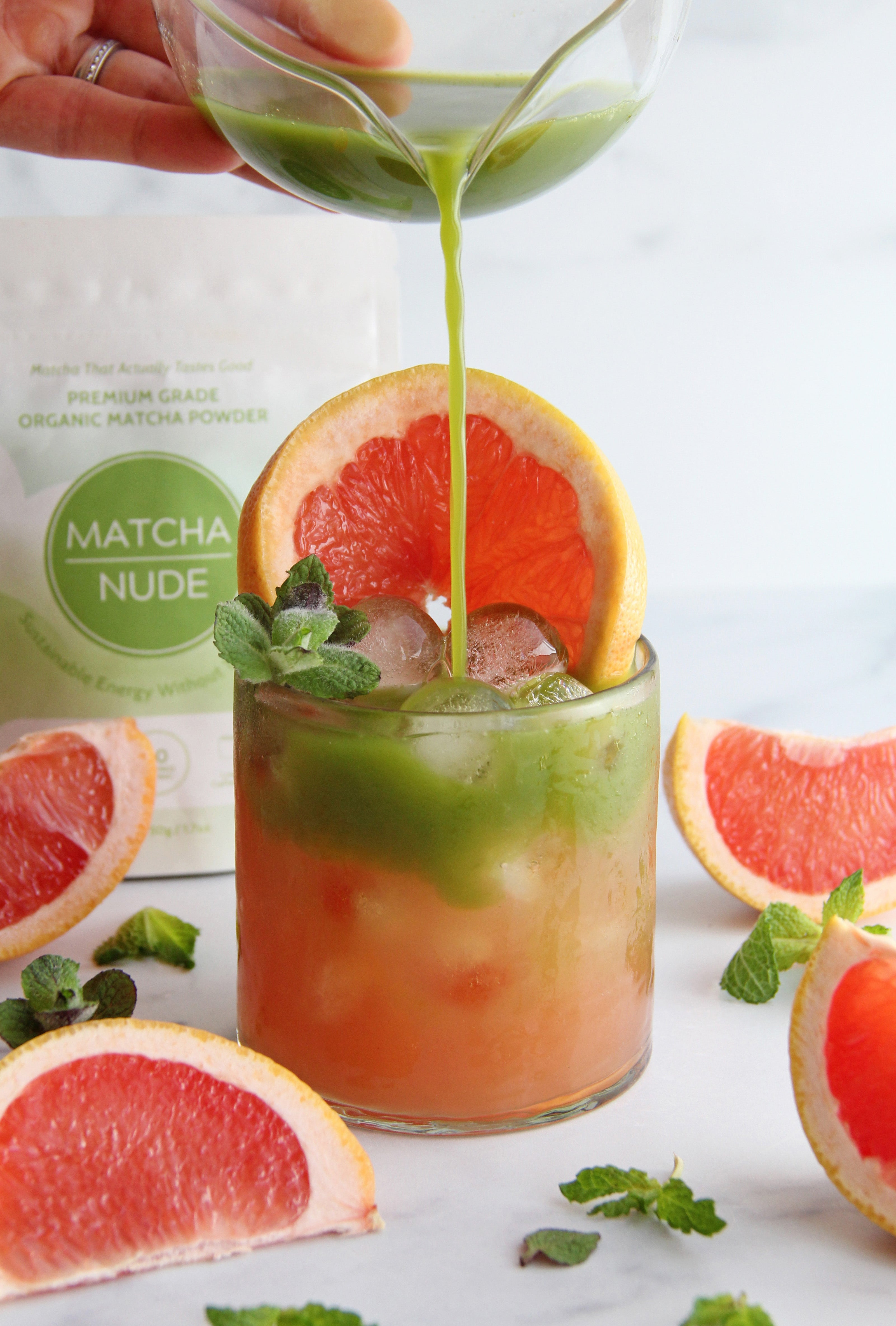 Matcha being poured over a grapefruit paloma drink with ice and mint