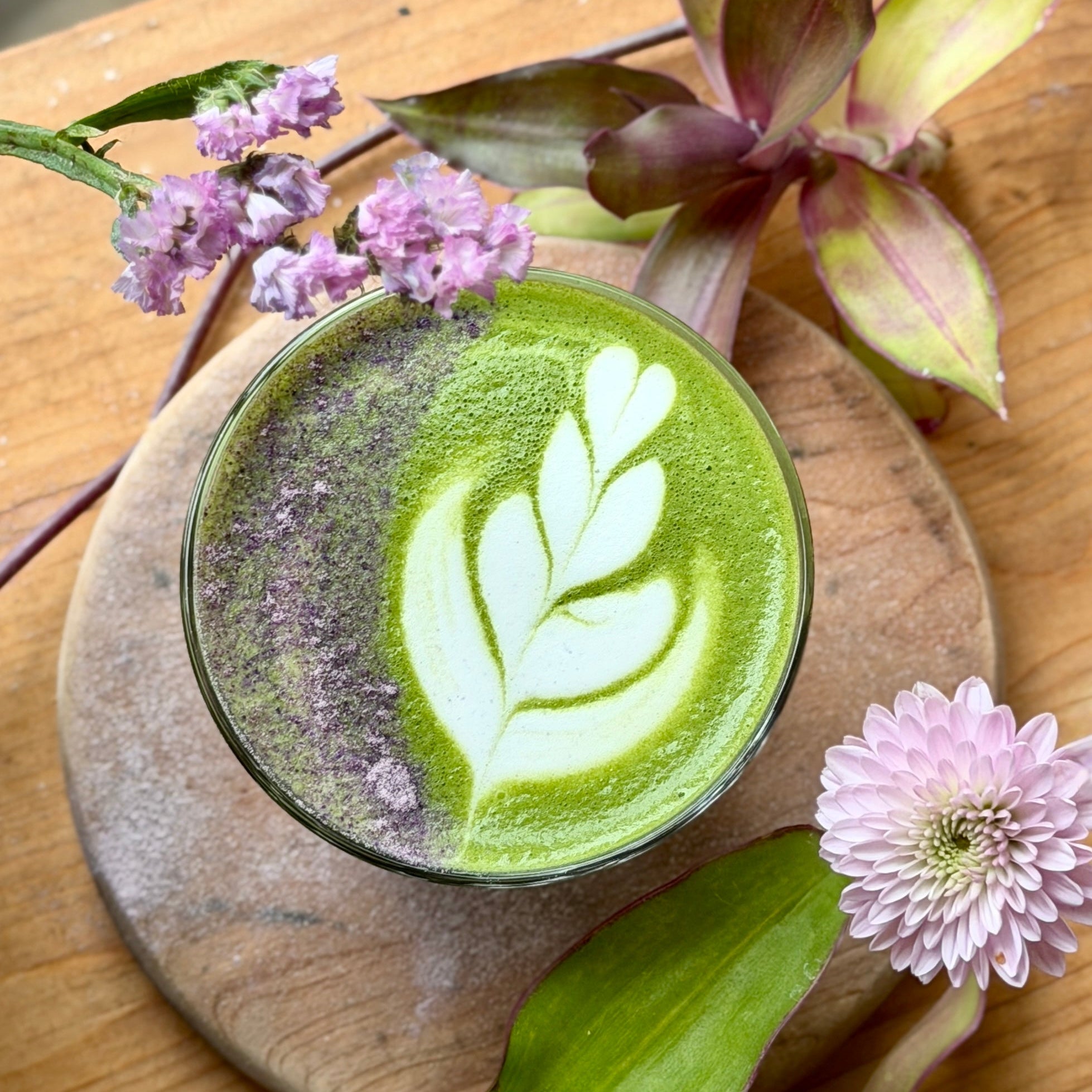Taro matcha latte with leaf art, topped with flowers on a wooden table