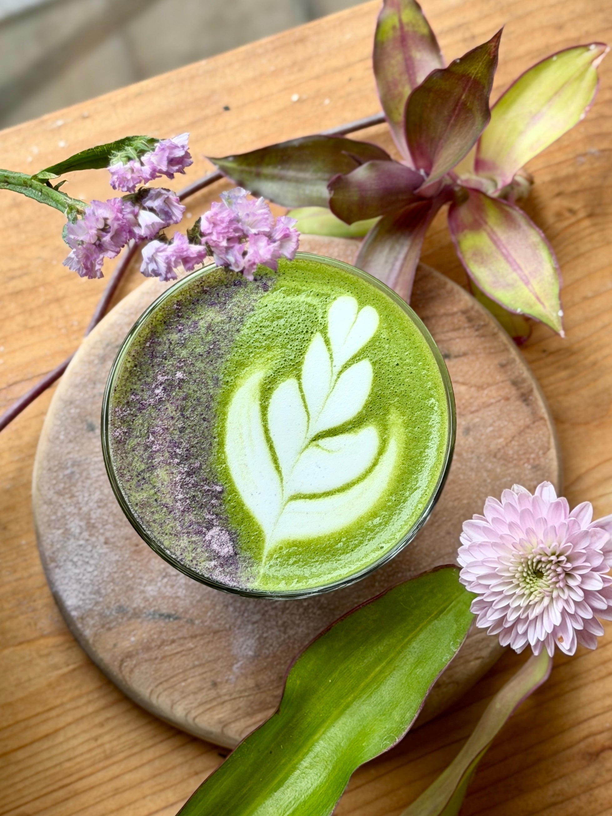 Taro matcha latte with leaf art, topped with flowers on a wooden table