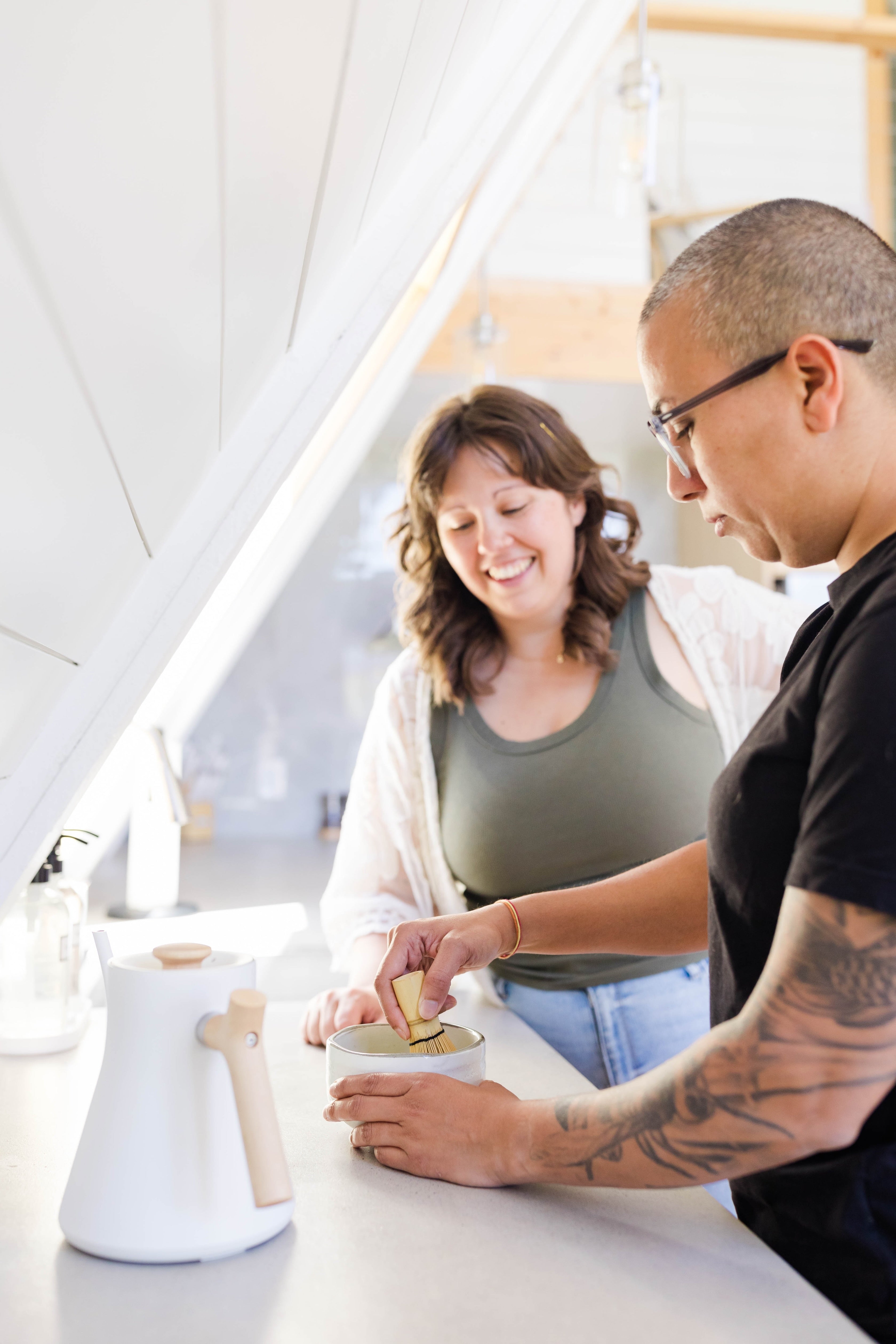 Two people whisking matcha together in a bright kitchen.