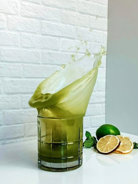 Matcha Highball Cocktail jumping out of glass with lemons and limes in background