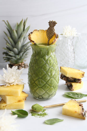 A vibrant green pineapple matcha smoothie served in a textured pineapple-shaped glass, topped with a fresh pineapple wedge and a fun pineapple spoon
