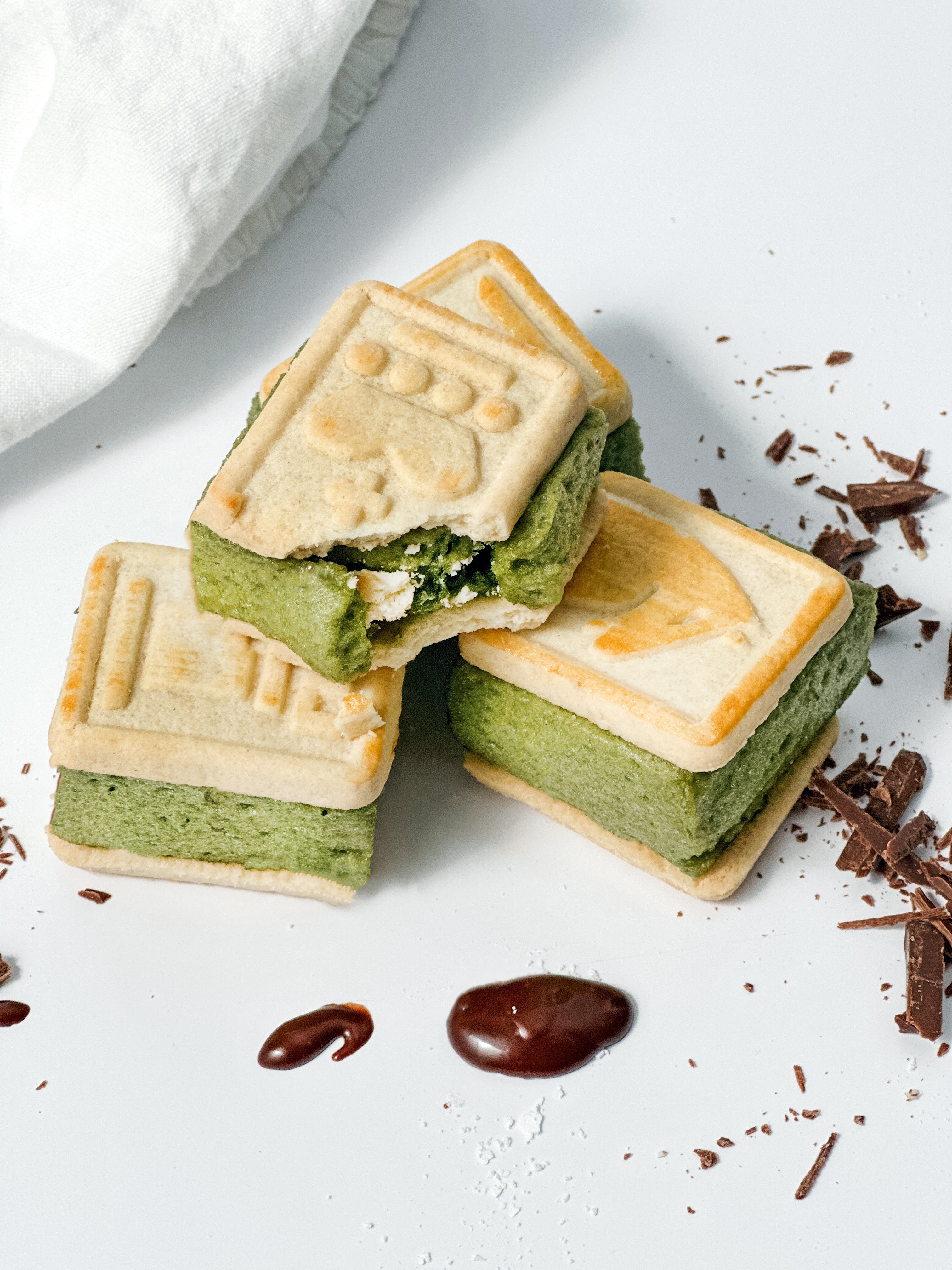 A stack of homemade Matcha Marshmallows with a vibrant green interior, set against a white background, surrounded by chocolate shavings and caramel drizzle. 🍵✨
