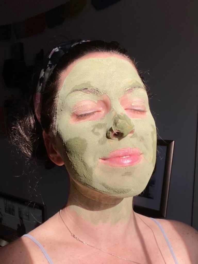 A woman with closed eyes enjoying the sunlight while wearing a homemade matcha face mask. The mask covers her face and neck in a smooth, even layer of rich green. She has a serene expression