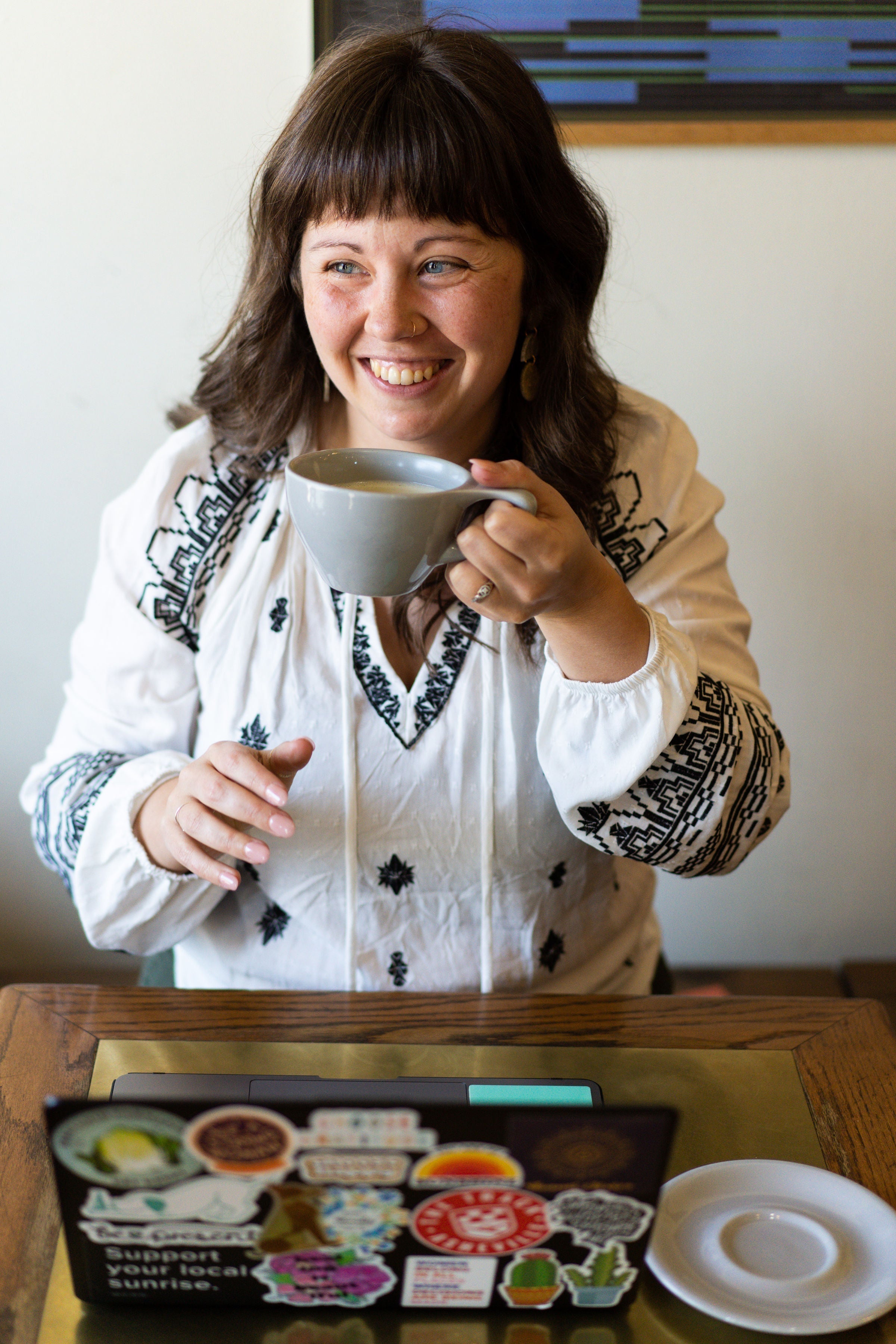 Person smiling while holding a warm matcha latte at a table while working.