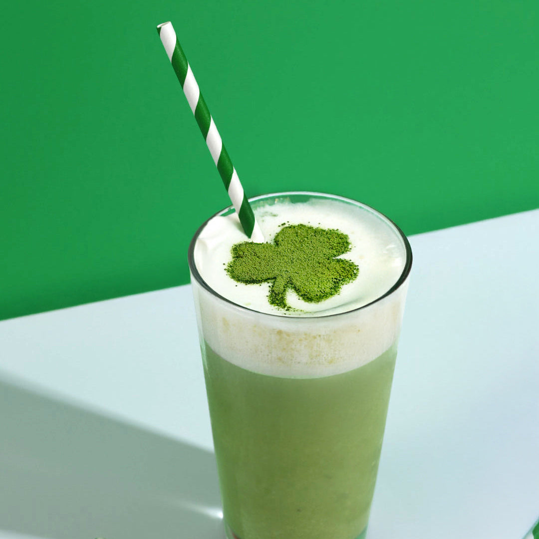 Shamrock Shake in a glass with a green and white striped straw and a shamrock shape made out of matcha powder on the top of the drink