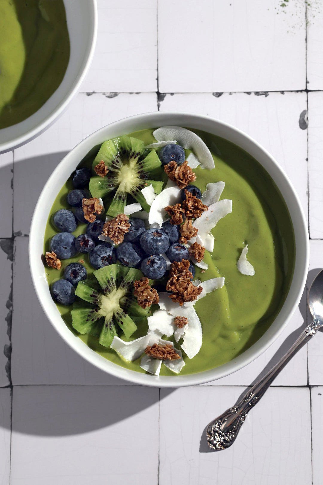 A green matcha smoothie bowl with blueberries, kiwis and granola as toppings