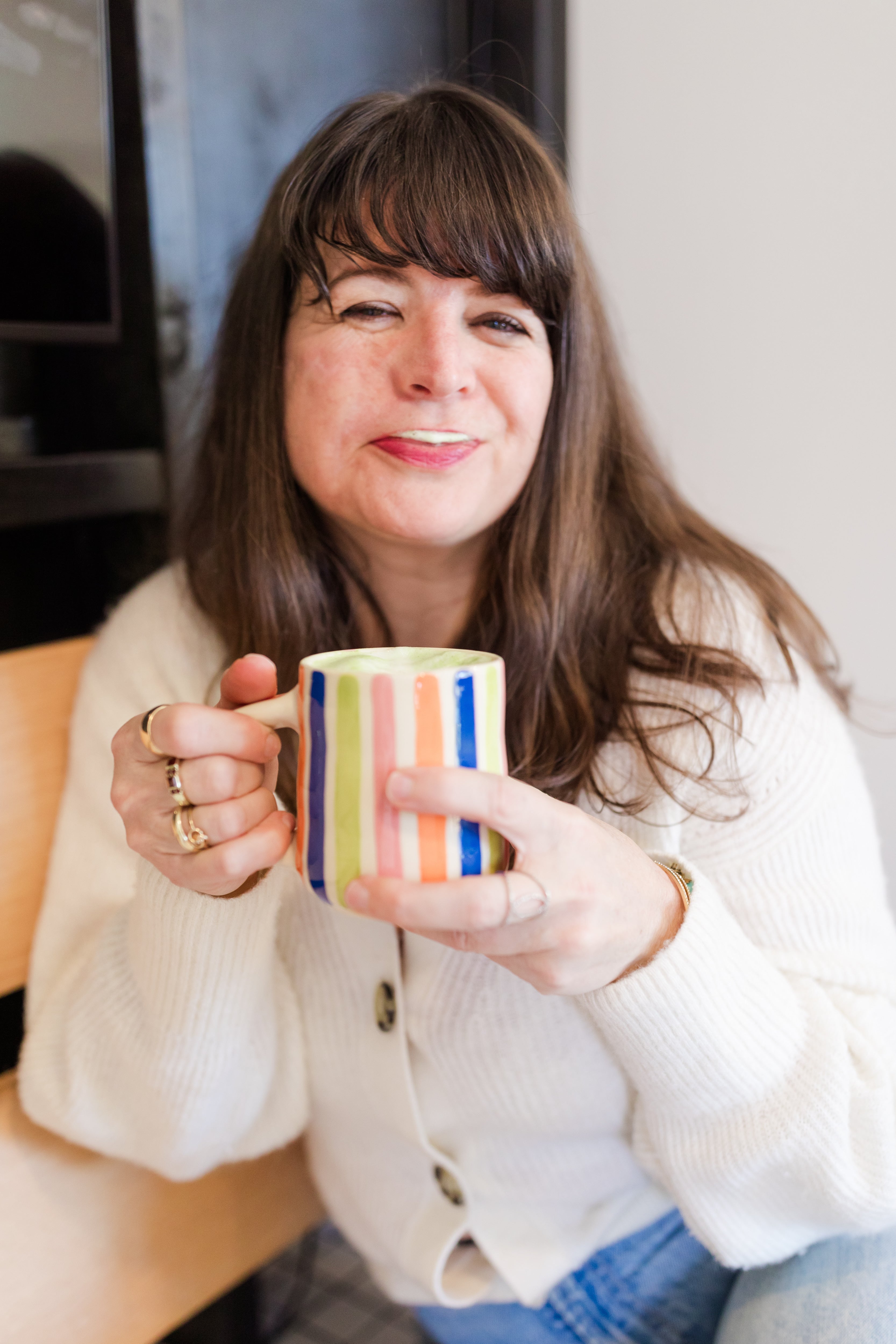 Person holding a colorful mug of matcha, smiling while seated indoors, representing a calm alternative to coffee