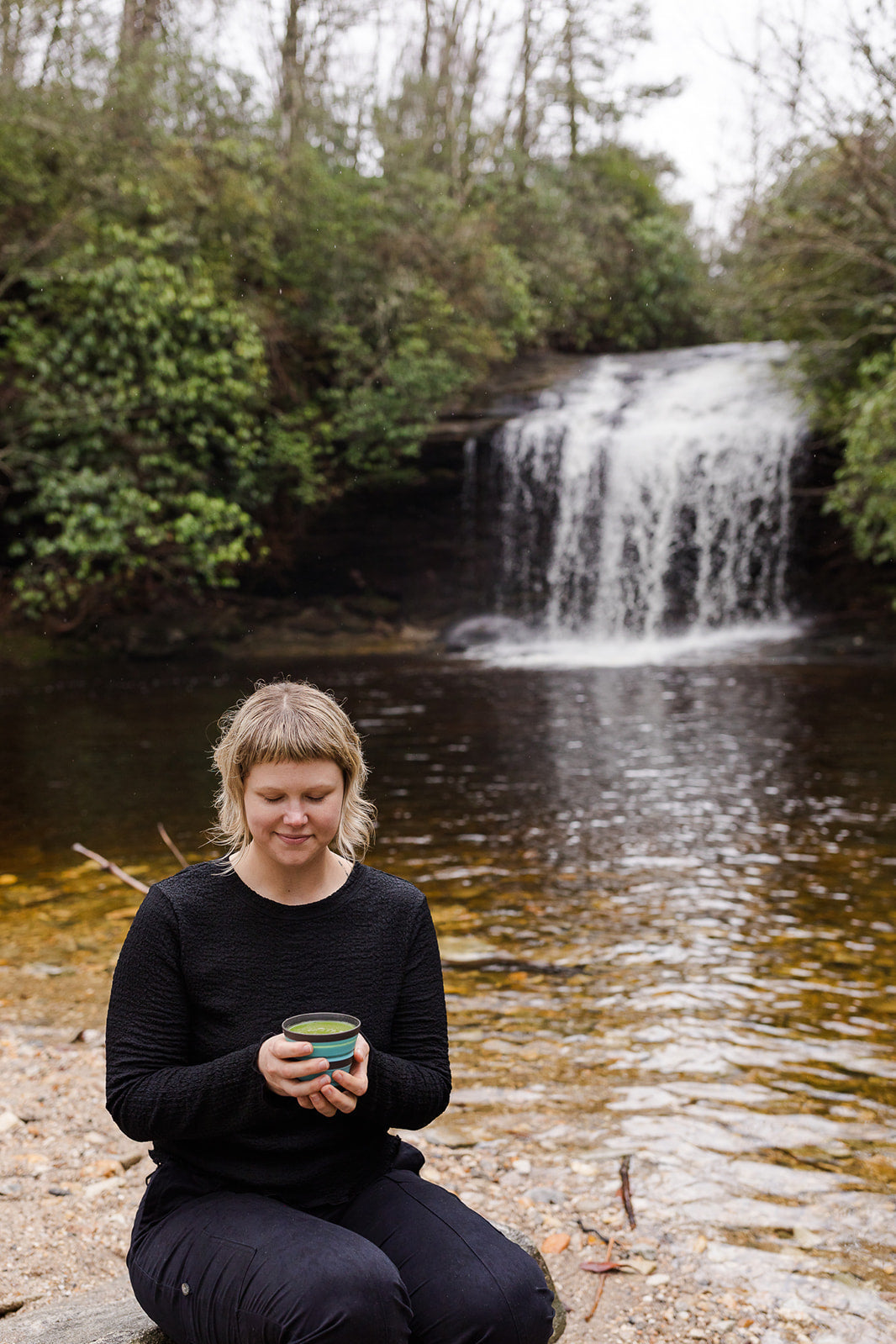 Person holding a cup of matcha in front of a waterfall