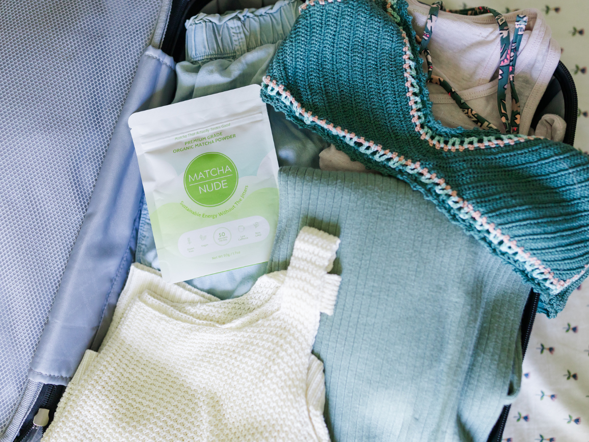 Matcha Nude 50 serving bag of premium grade organic matcha that actually tastes good. Sustainable Energy without the jitters in an open suitcase with feminine clothes