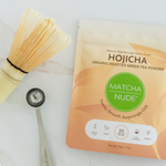 Flat lay of Matcha Nude organic hojicha powder with bamboo whisk and matcha spoon