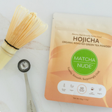 Flat lay of Matcha Nude organic hojicha powder with bamboo whisk and matcha spoon