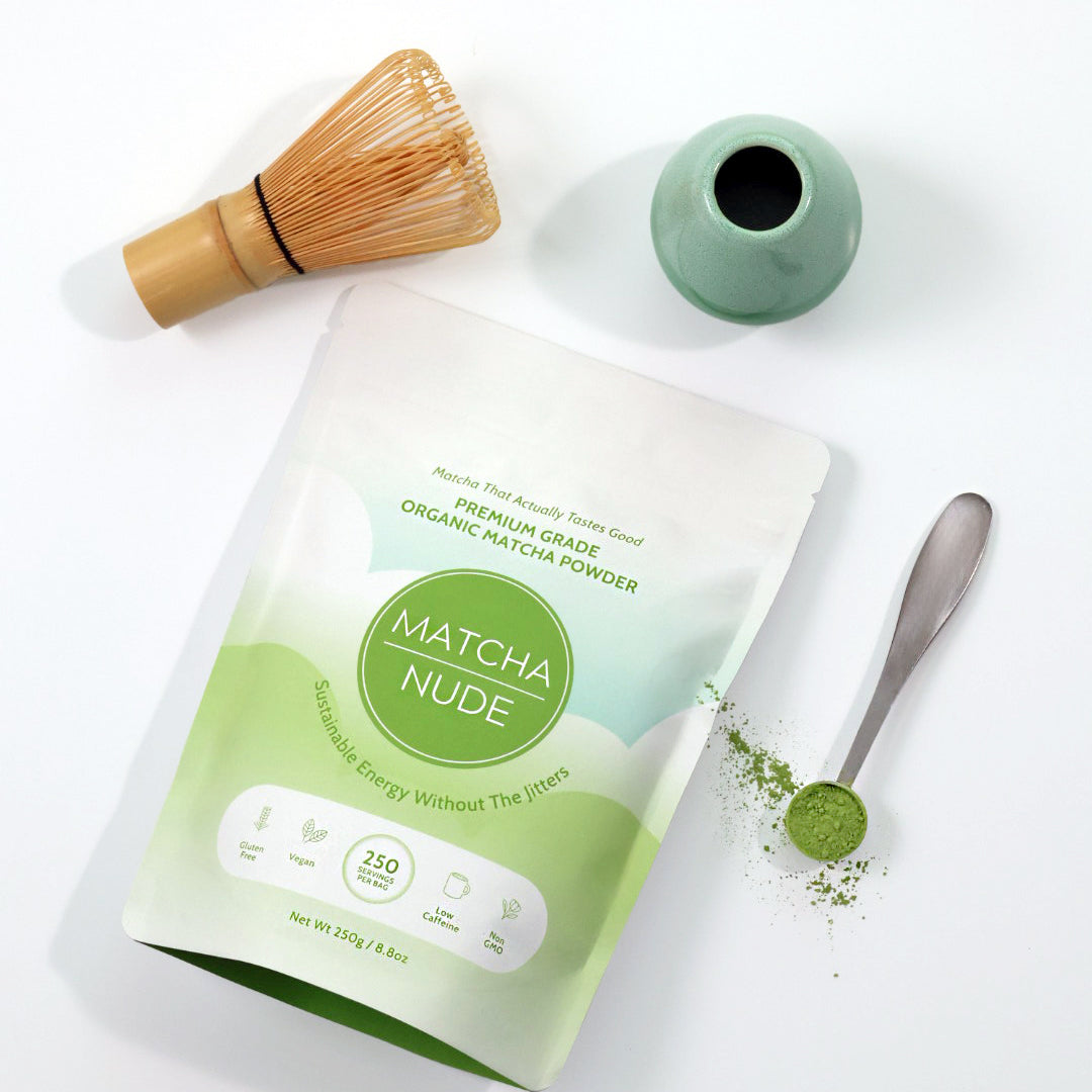 Premium organic matcha powder by Matcha Nude showcased with a traditional bamboo whisk and a green ceramic whisk holder. This sustainable matcha brand offers clean energy without jitters, featuring gluten-free, vegan, and non-GMO benefits. Perfect for matcha enthusiasts seeking quality and eco-friendly choices