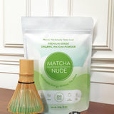Matcha Nude’s premium organic matcha powder displayed in compostable packaging alongside a bamboo whisk and a metal measuring spoon. Highlighting the brand's commitment to sustainability and clean energy, this gluten-free, vegan, and low-caffeine matcha is ideal for mindful wellness routines.

