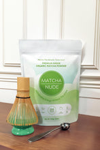 Load image into Gallery viewer, Matcha Nude’s premium organic matcha powder displayed in compostable packaging alongside a bamboo whisk and a metal measuring spoon. Highlighting the brand&#39;s commitment to sustainability and clean energy, this gluten-free, vegan, and low-caffeine matcha is ideal for mindful wellness routines.
