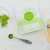 Overhead view of Matcha Nude Premium Matcha powder with bamboo whisk and matcha spoon