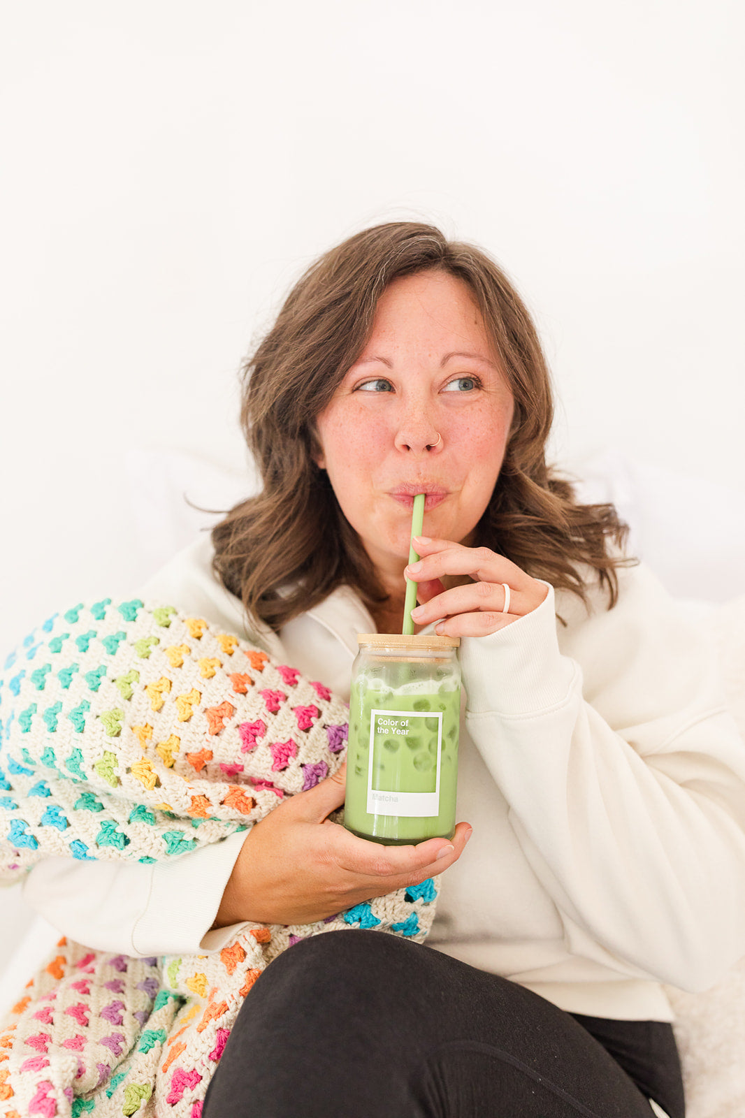 Woman enjoying an iced matcha latte while relaxing with a colorful blanket.