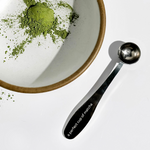 A perfect cup of matcha spoon next to a bowl with matcha powder