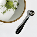 A perfect cup of matcha spoon next to a bowl with matcha powder